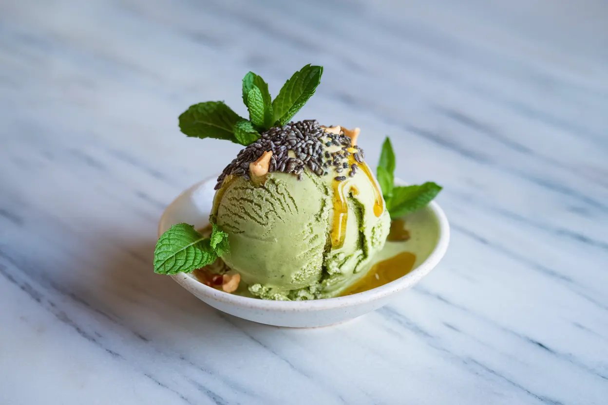 Matcha ice cream with chia seeds, mint leaves, and honey drizzle served in a white dish